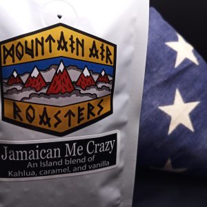 one pound mountain air roasters, jamaican coffee bag. the beach with sand, the ocean with small rustling waves in an isolated cove with pink and purple clouds of evening sunlight