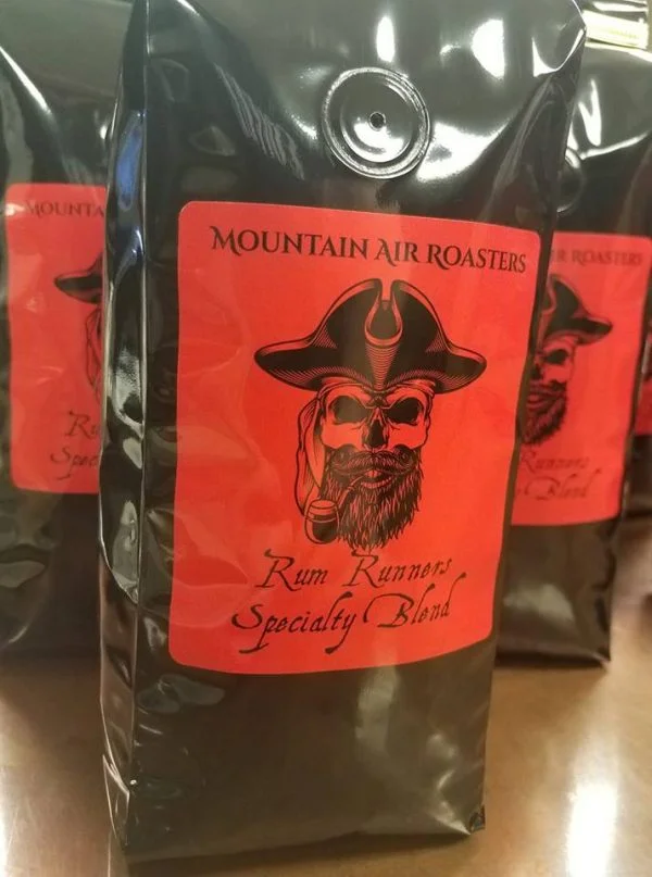 Mountain Air Roasters Rum Runners Specialty blend, black bag, big red sticker and a black pirate skull with pirate captains hat smoking an old cob pipe